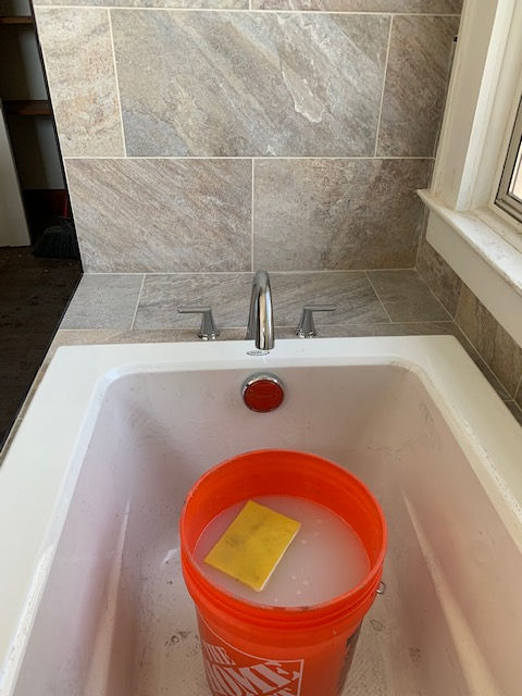 A bathtub with a bucket of water and a sponge in it