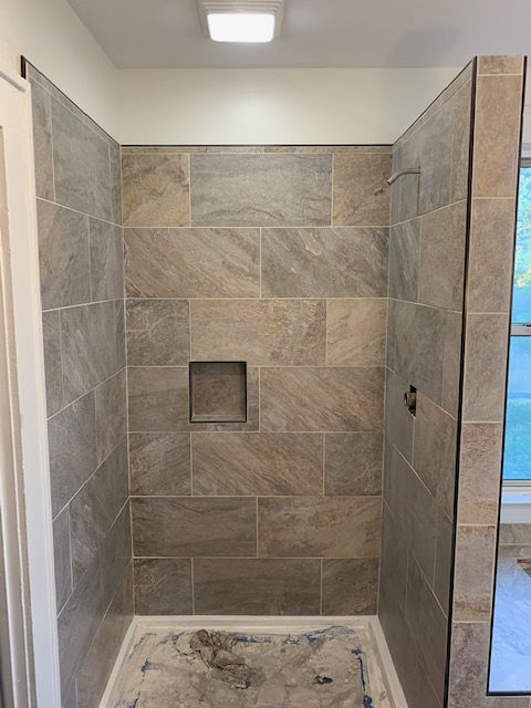 A bathroom with a walk in shower with tiled walls and a window.