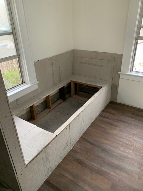 There is a bench in the corner of a room next to a window.