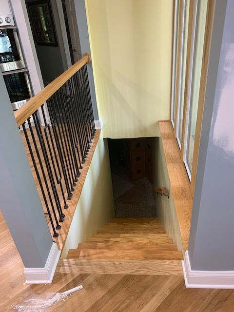 A wooden staircase with a black railing leading to a basement.