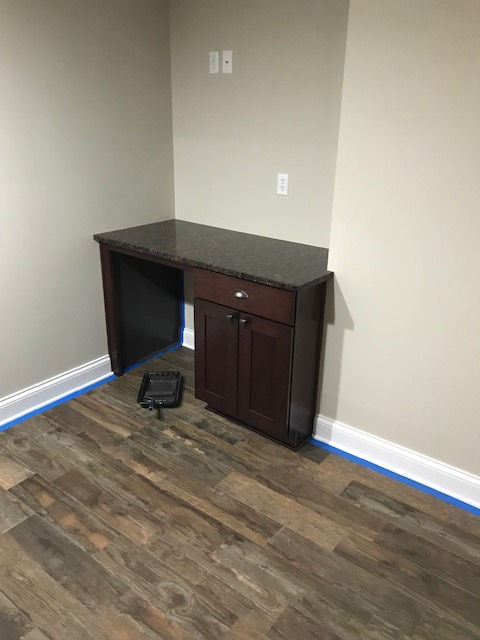 There is a desk in the corner of a room with hardwood floors.