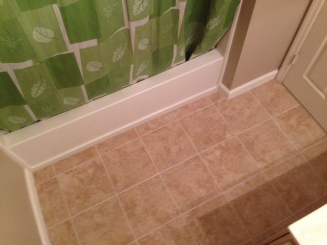 A bathroom with a green shower curtain and a tiled floor