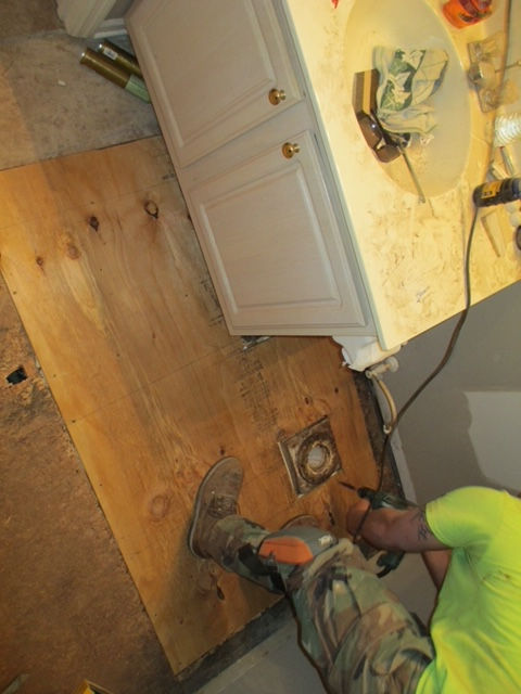 A man in a green shirt is working on a bathroom floor