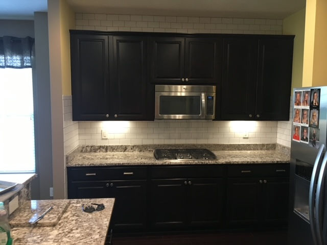 A kitchen with black cabinets , granite counter tops , a stove , microwave and refrigerator.