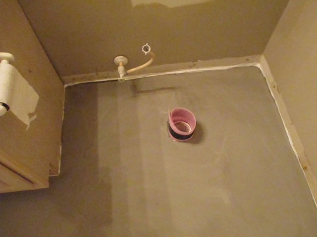 A pink bowl is sitting on the floor of a bathroom.