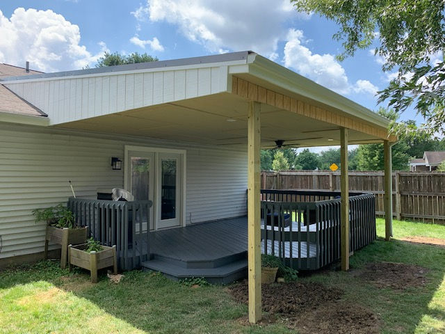 There is a covered deck in the backyard of a house.