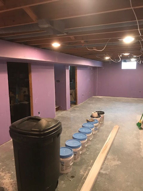 A row of buckets are lined up in a basement with purple walls.