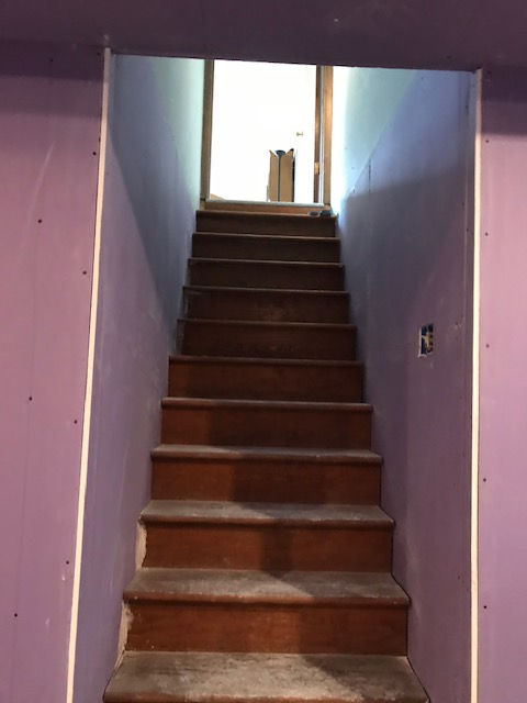 A set of wooden stairs leading up to a purple wall