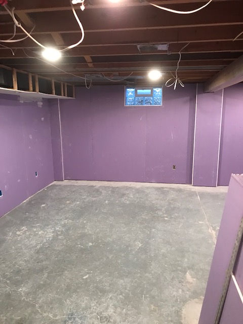 An empty basement with purple walls and a concrete floor.