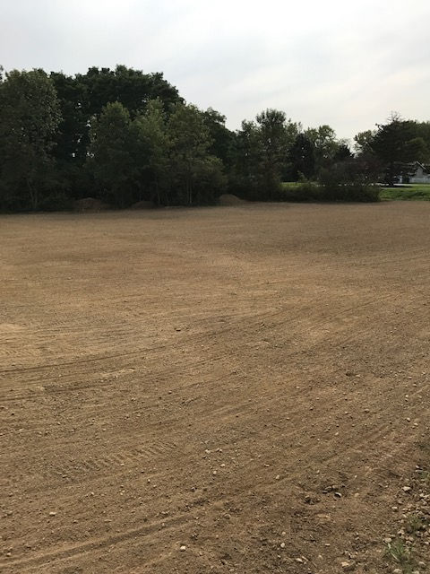 A large dirt field with trees in the background.
