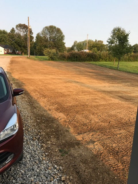 A red car is parked on the side of a dirt road.