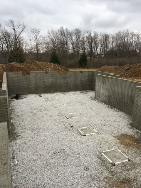A concrete basement under construction with gravel and trees in the background.