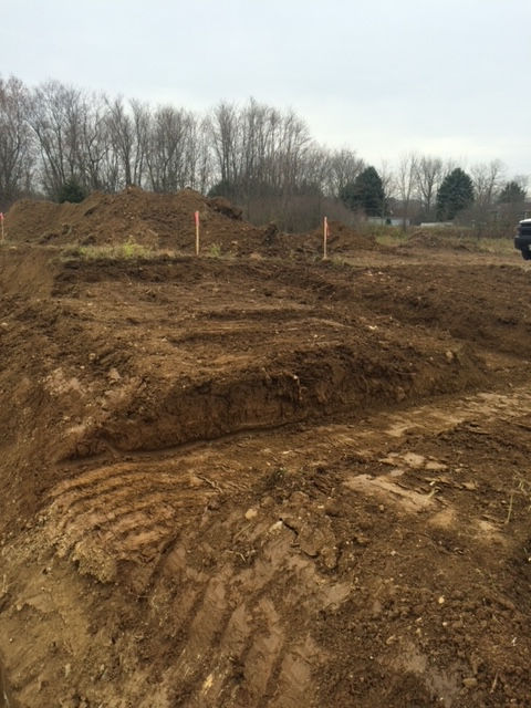 A large pile of dirt in a field with trees in the background.