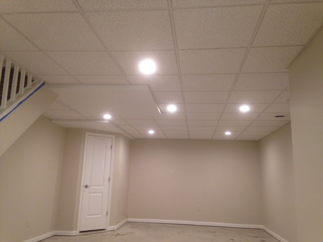 An empty basement with a tiled ceiling and stairs.