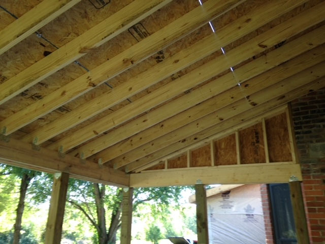 A wooden porch with a brick wall and trees in the background