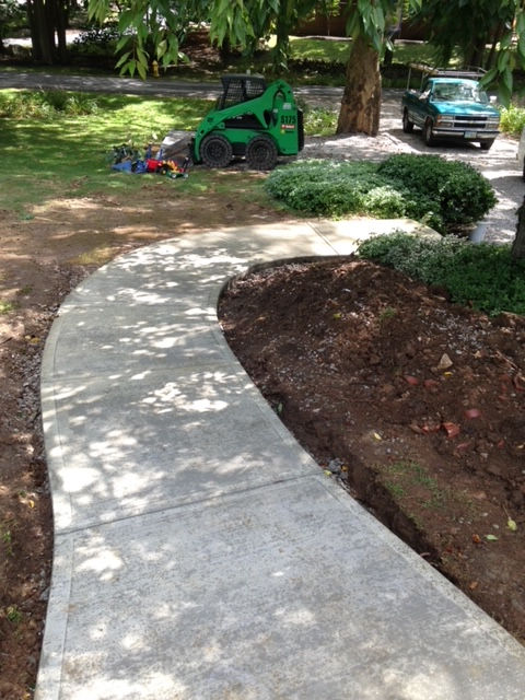 A green tractor is parked on the side of a sidewalk
