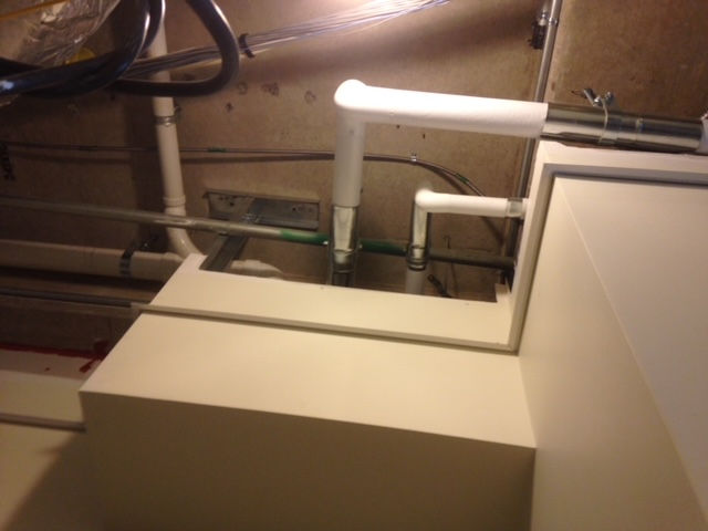 A corner of a room with white pipes and wires