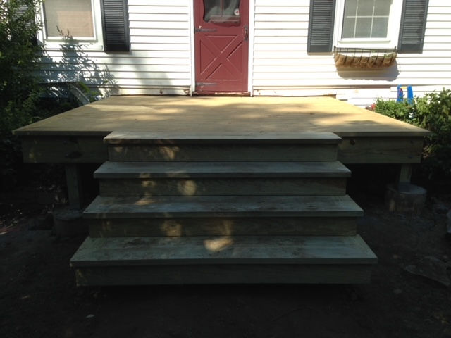 A wooden deck with stairs in front of a white house