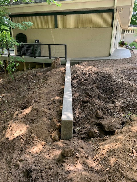 A concrete wall is being built in the dirt in front of a house.
