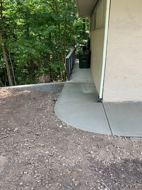 A concrete walkway leading to a house with trees in the background.