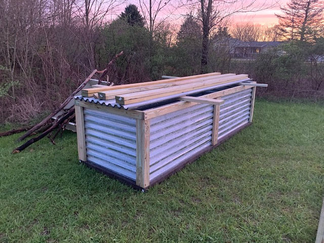 A shed made of corrugated metal and wood is sitting in the grass.