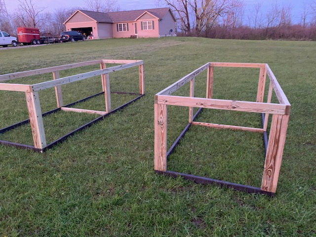 Two wooden frames are sitting in a grassy field in front of a house.