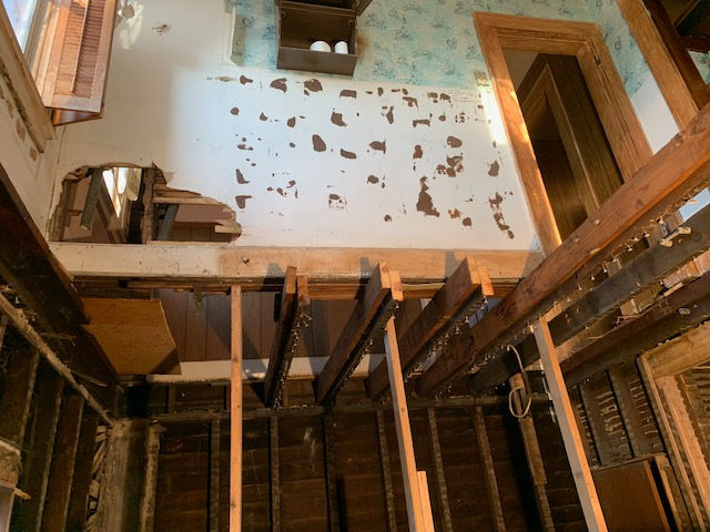 A room with a hole in the ceiling and wooden beams.