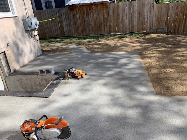 A lawn mower is sitting on a concrete patio next to a wooden fence.