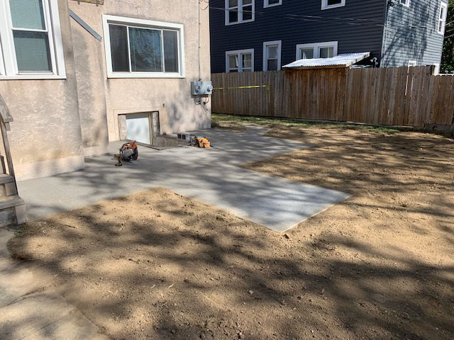 A concrete patio is being built in the backyard of a house.