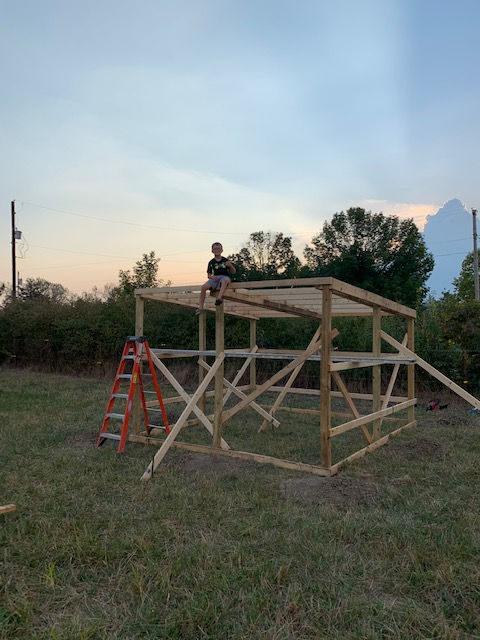 A man is sitting on top of a wooden structure in a field.