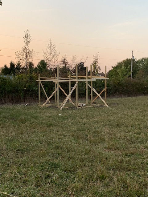 A wooden structure is sitting in the middle of a grassy field.