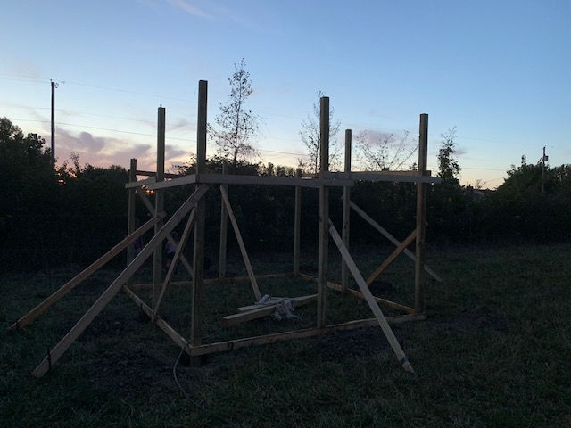 A wooden structure is being built in a field at sunset