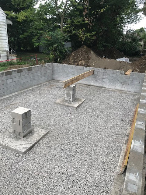 A concrete foundation is being built in a backyard with gravel and bricks.