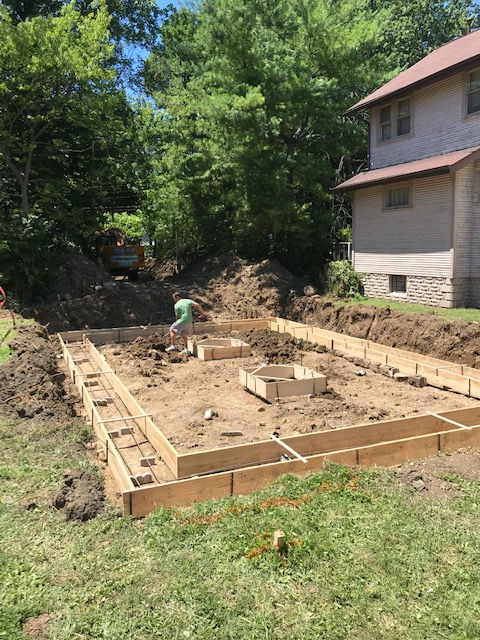 A man is working on a concrete foundation in front of a house.