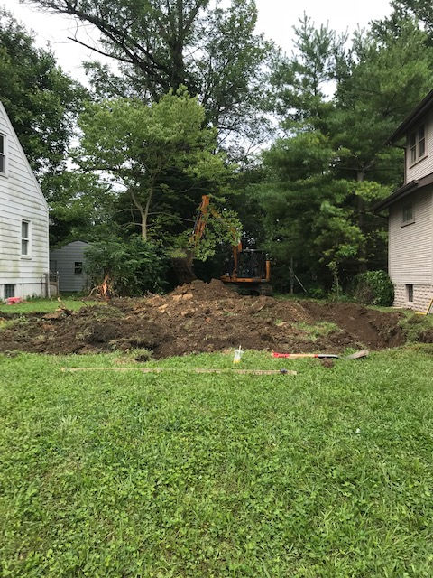 A large excavator is digging a hole in the backyard of a house.