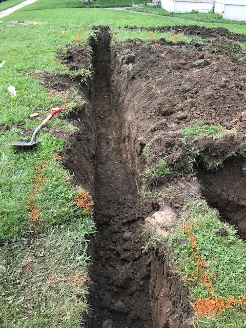 A trench is being dug in the grass with a shovel.