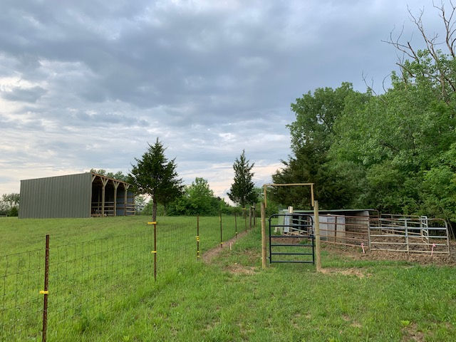 A large grassy field with a fence and a barn in the background.