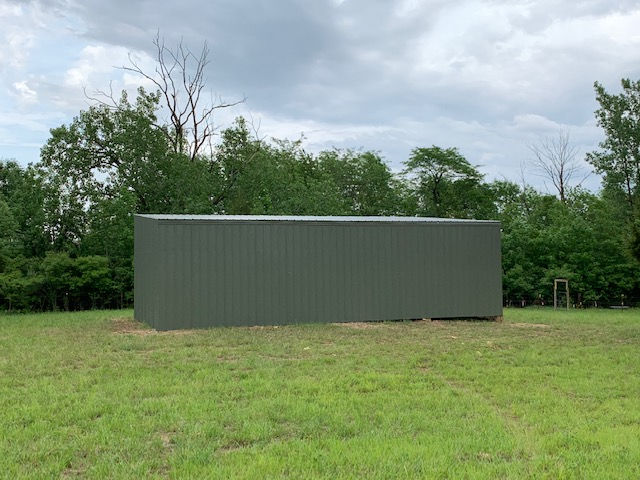 A large metal building is sitting in the middle of a grassy field.