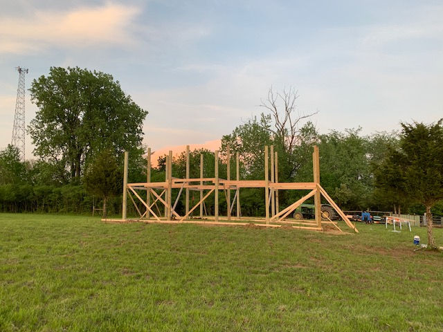 A large wooden structure is being built in a grassy field.