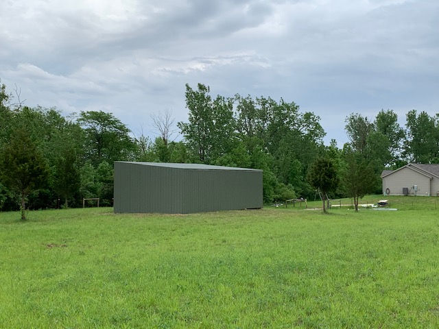 A large green building is sitting in the middle of a grassy field.