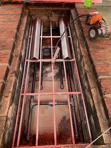 A brick wall with a metal fence and pipes in it.