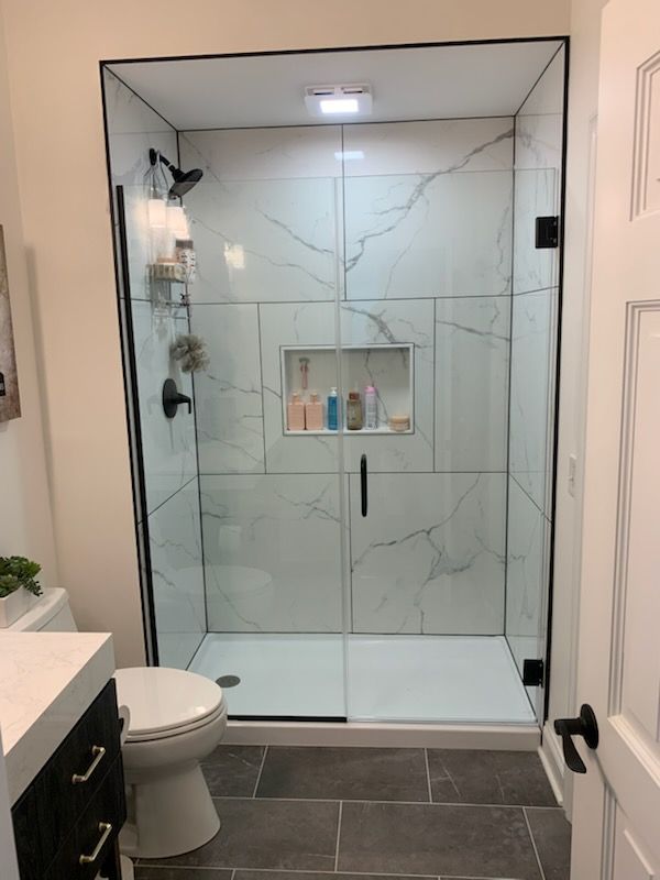 Modern bathroom with marble-tiled shower, black hardware, glass doors, and a built-in shelf.