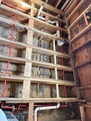 A vertical wall frame showing white PVC drainage pipes alongside red and blue PEX plumbing lines in an unfinished room.