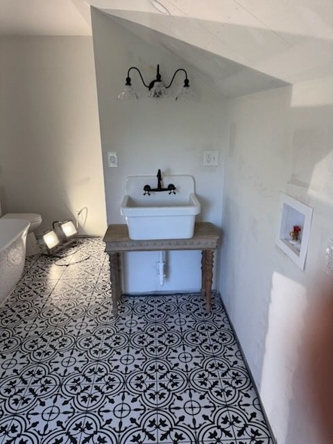 Bathroom with white walls, patterned floor, and a sink on a wooden stand. A clawfoot tub is partially visible.