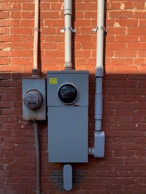 An electrical box is attached to a brick wall
