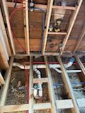 Unfinished ceiling framing showing white PVC plumbing pipes and red PEX water lines between exposed wooden joists.
