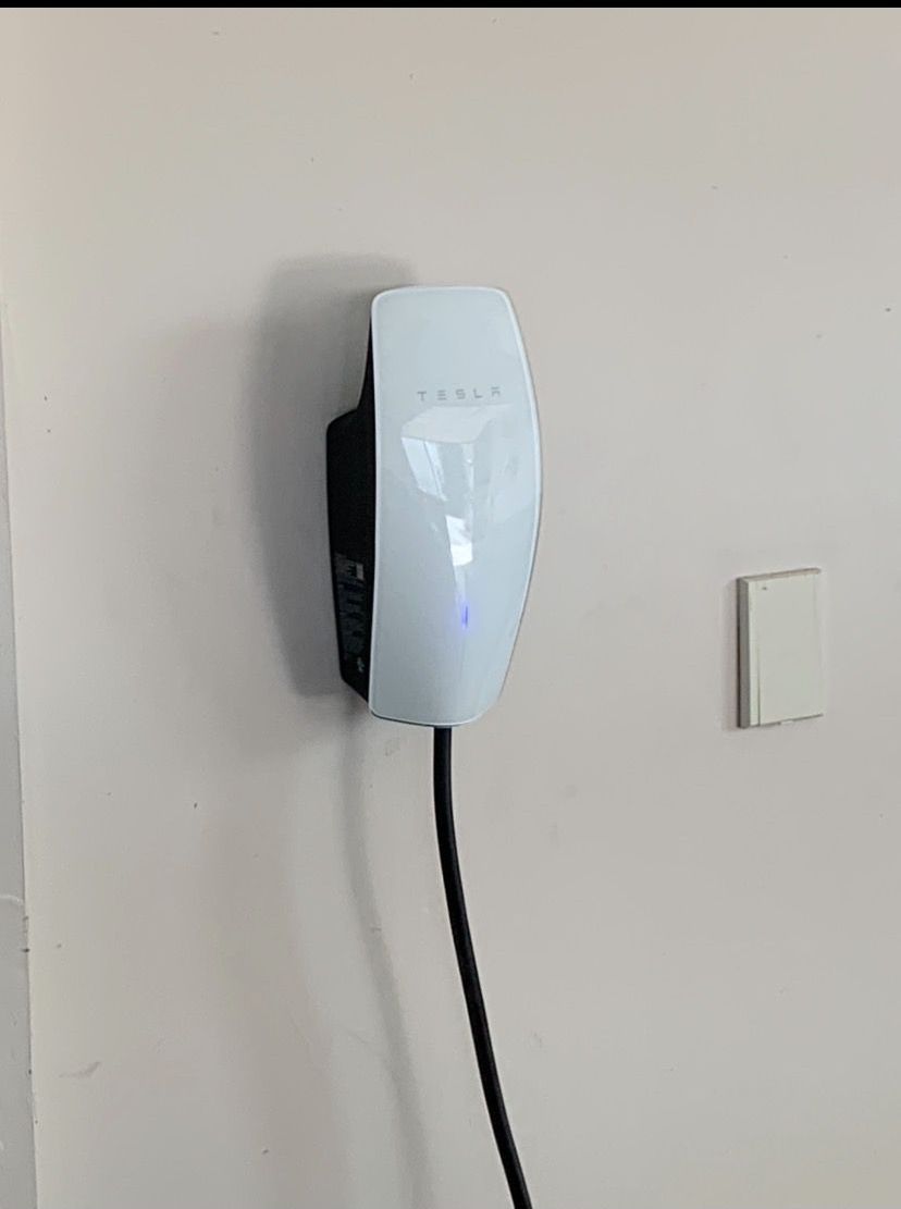 A tesla charging station is plugged into a wall.