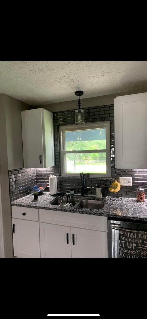 A kitchen with white cabinets , a sink , and a window.