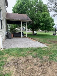 A house with a covered patio and a gravel driveway in front of it.