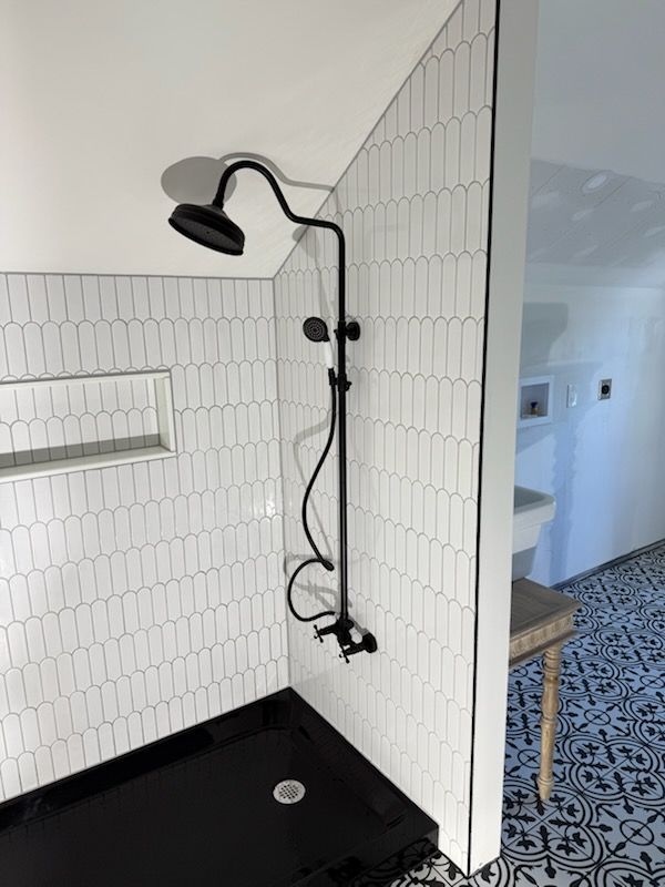 Black shower fixture in a white-tiled shower stall with a black base.  Part of a bathroom.